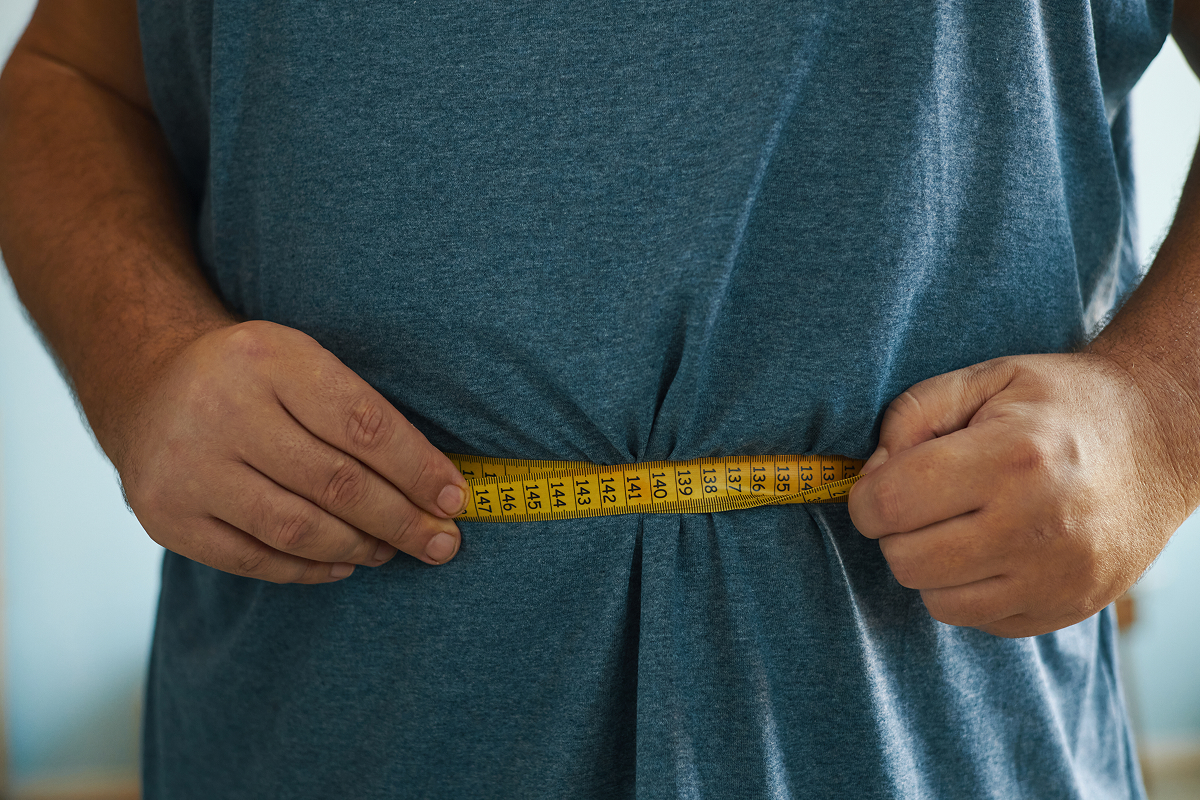 A man using a measuring tape to measure his stomach